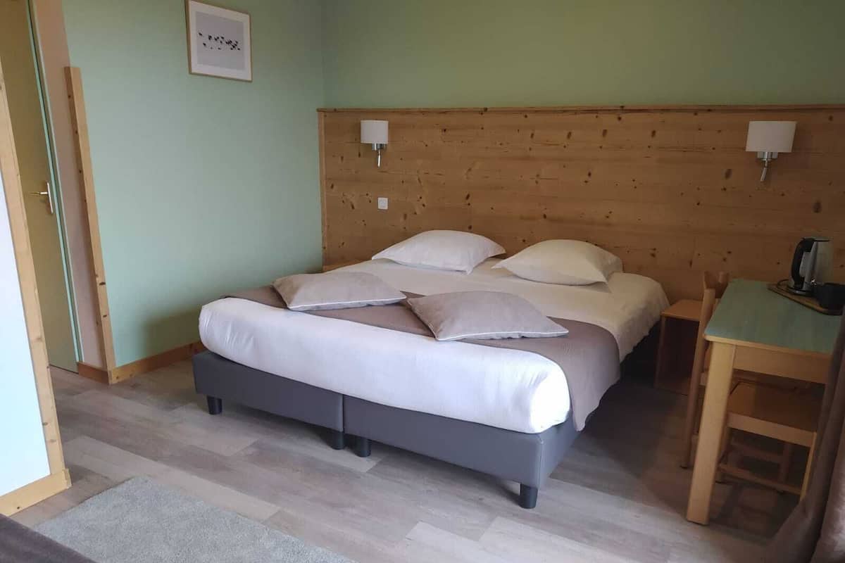 A bedroom with a bed, pillows, a bedside table, a lamp, and a wooden headboard.