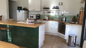 A kitchen with a central island, white cabinets, a microwave, and a stove. There are stools at the island and a trash can near the stove. - CONTEMPORARY VILLA IN PROVENCE CAMPAIGN, AIX EN PROVENCE, AUBAGNE, MARSEILL (Peypin)