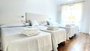 Habitació d'hotel amb tres llits, bigues de fusta al sostre i una finestra gran amb cortines.