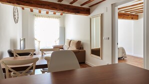 Una habitació amb taula de menjador de fusta, cadires, un sofà i un mirall gran.