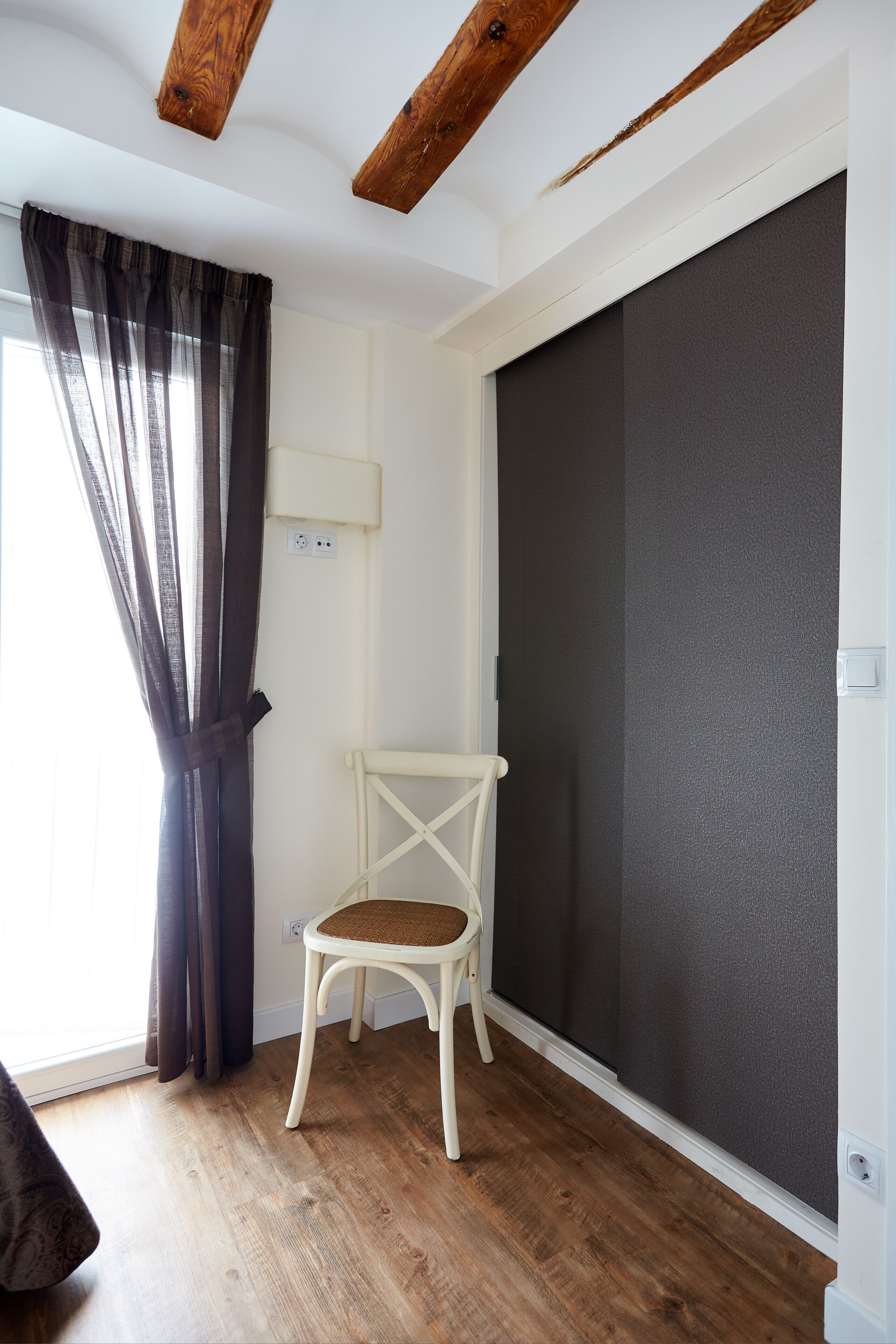 A room with a wooden floor, a white chair with a cushion, a dark curtain, and a large grey sliding door.
