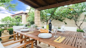 Zona pranzo all'aperto con tavolo in legno apparecchiato per quattro persone, circondata da vegetazione e un muro in pietra.