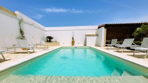 Una piscina rettangolare con acqua cristallina e trasparente, circondata da pareti bianche e pavimento in pietra.