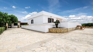 Un edificio bianco con facciata in pietra, una piccola area giardino con piante in vaso e un cortile pavimentato.