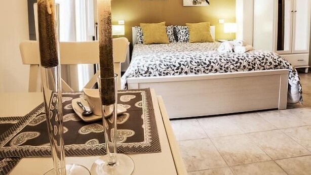 Un dormitorio con cama, mesitas de noche, armario y ventana con cortinas.