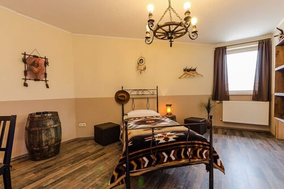 A bedroom with a bed, a chandelier, a wooden barrel, and a radiator.