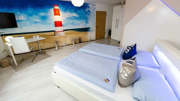 A modern hotel room with a bed, a desk, and a large mural of a lighthouse. - Hotel Rosenhof (Isenbuttel)