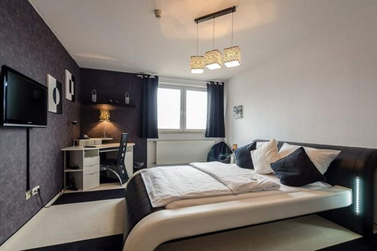 A modern bedroom with a bed, desk, and TV.