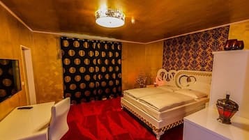 A hotel room with a bed, a desk, a chair, a mirror, and a patterned wall.