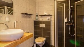 A modern bathroom with a large white sink, a toilet, and a glass-enclosed shower area. - Hotel Rosenhof (Isenbuttel)