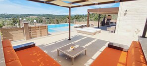 A rooftop patio with a swimming pool, outdoor seating, and a view of the countryside.