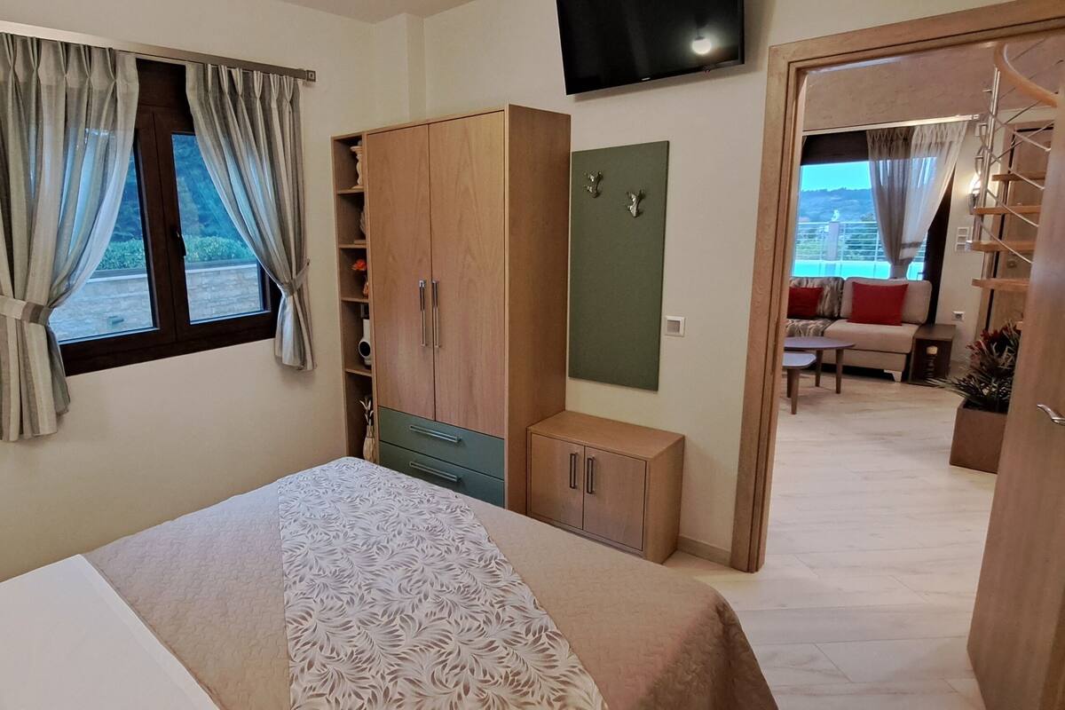A hotel room with a bed, a wardrobe, a small cabinet, a TV mounted on the wall, and a view of the outside through a window.