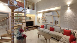 En rummelig opholdsstue med en moderne trappe, et fladskærms-tv, en sofasæt og dekorative reoler.