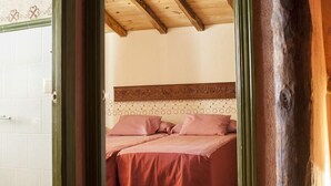 Ein Schlafzimmer mit Holzbalkendecke, einem Bett mit roter Bettwäsche und einer weißen Fliesenwand.