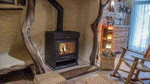 A rustic interior with a wood-burning stove, stone walls, and a wooden chair.