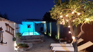 A stone-paved outdoor area with a pool, lounge chairs, and string lights.
