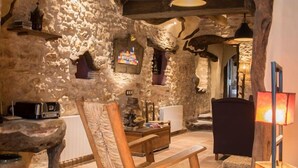 A rustic interior with exposed stone walls, wooden beams, a stone bench, and a woven basket.