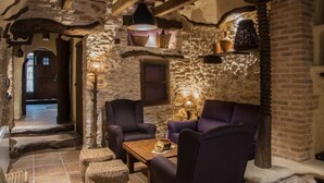 A rustic interior with stone walls, wooden beams, and a cozy seating area with two armchairs and a table.