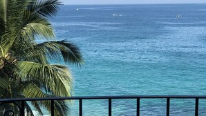 Un balcon avec des fauteuils confortables donnant sur l’océan, un palmier et une vue sur la mer.