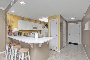 Une cuisine moderne avec des meubles blancs, un îlot central doté de tabourets et un mur d’accent jaune.