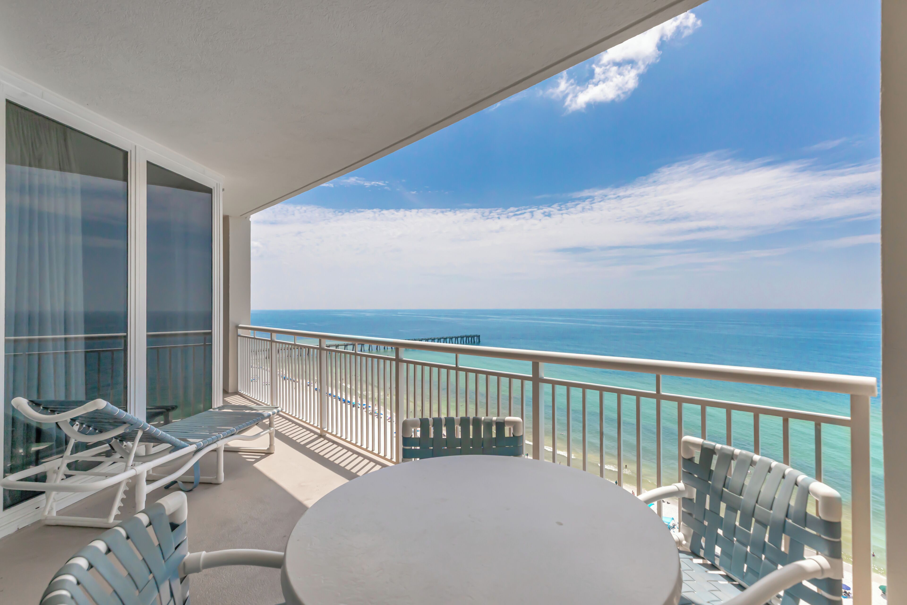 A balcony with a view of the ocean, a table, and two chairs.