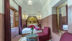 A bedroom with a bed, a bedside table with a vase, a chair, a mirror, and a decorative wall piece. - RIAD DAR YEMA (marrakech)