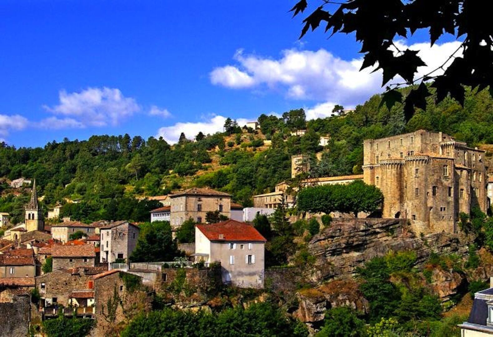 A historic town with a prominent castle on a hill, surrounded by lush greenery and traditional buildings.