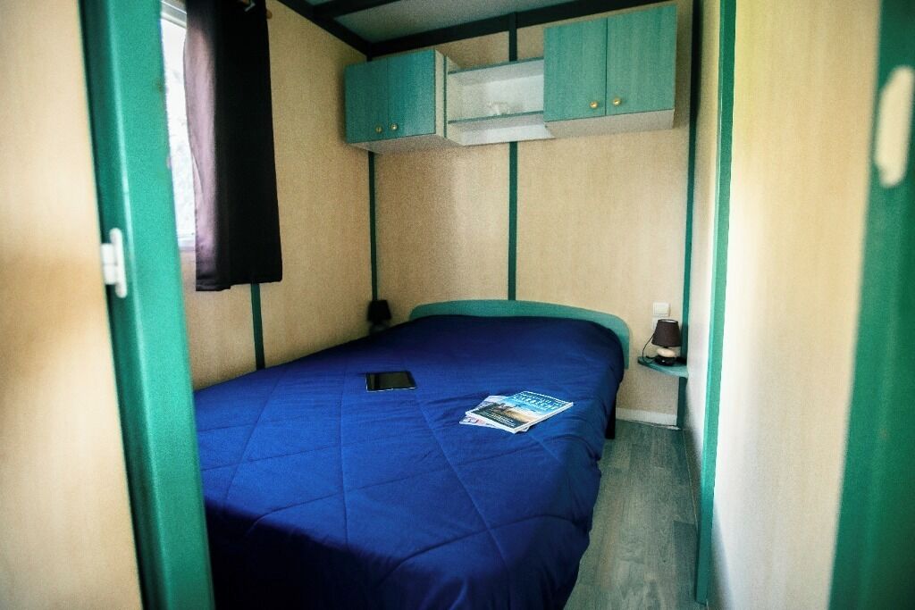 A small, narrow room with a single bed, a window, and a kitchenette area.