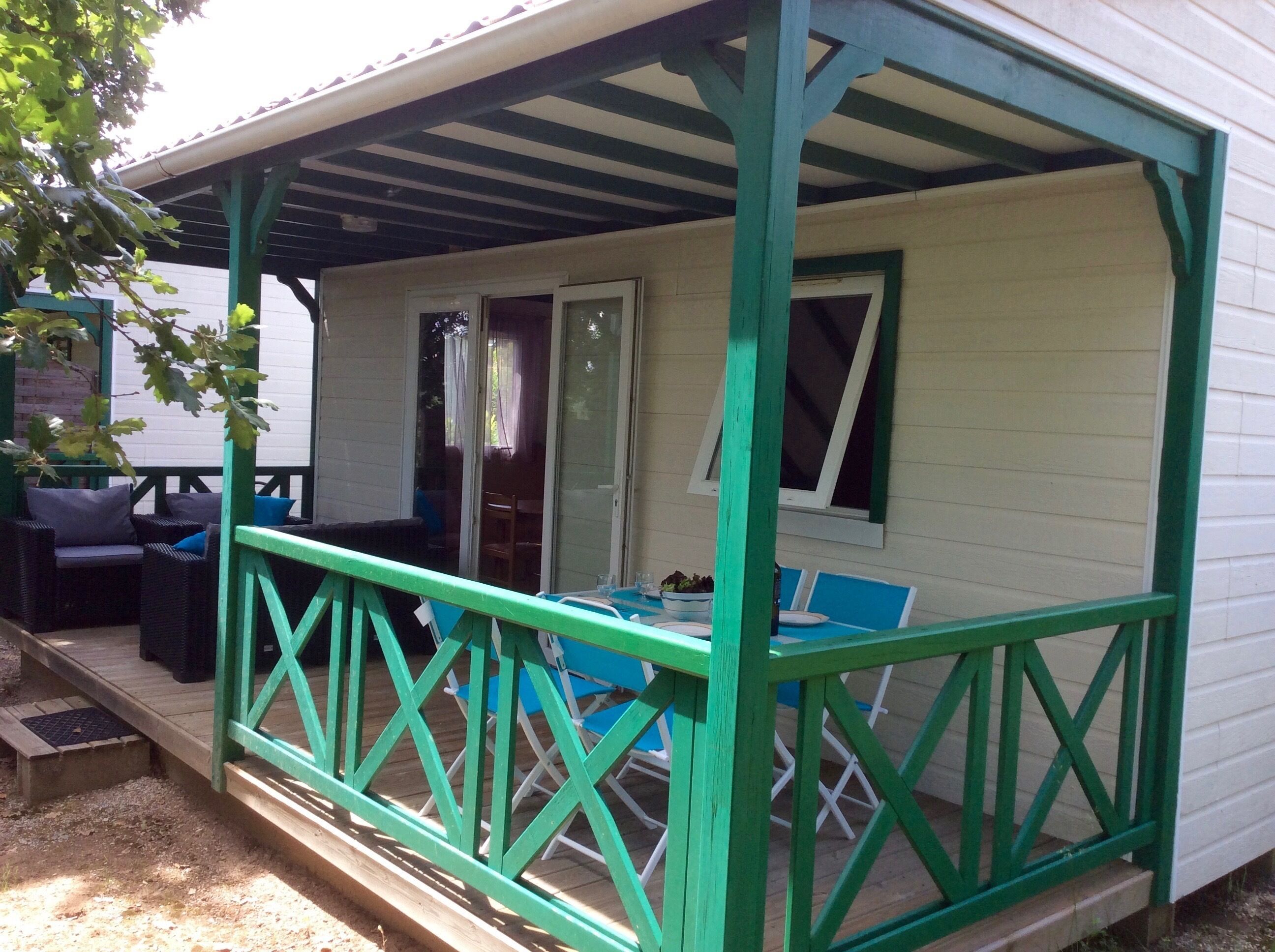 Een overdekte veranda met een groene balustrade, zitplaatsen buiten en een tafel met stoelen.