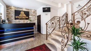 Modernilla designilla varustettu hotellin vastaanottoalue, johon kuuluu vastaanottotiski, koristeellisilla metallikaiteilla varustetut portaat ja seinälle asennettu televisio.
