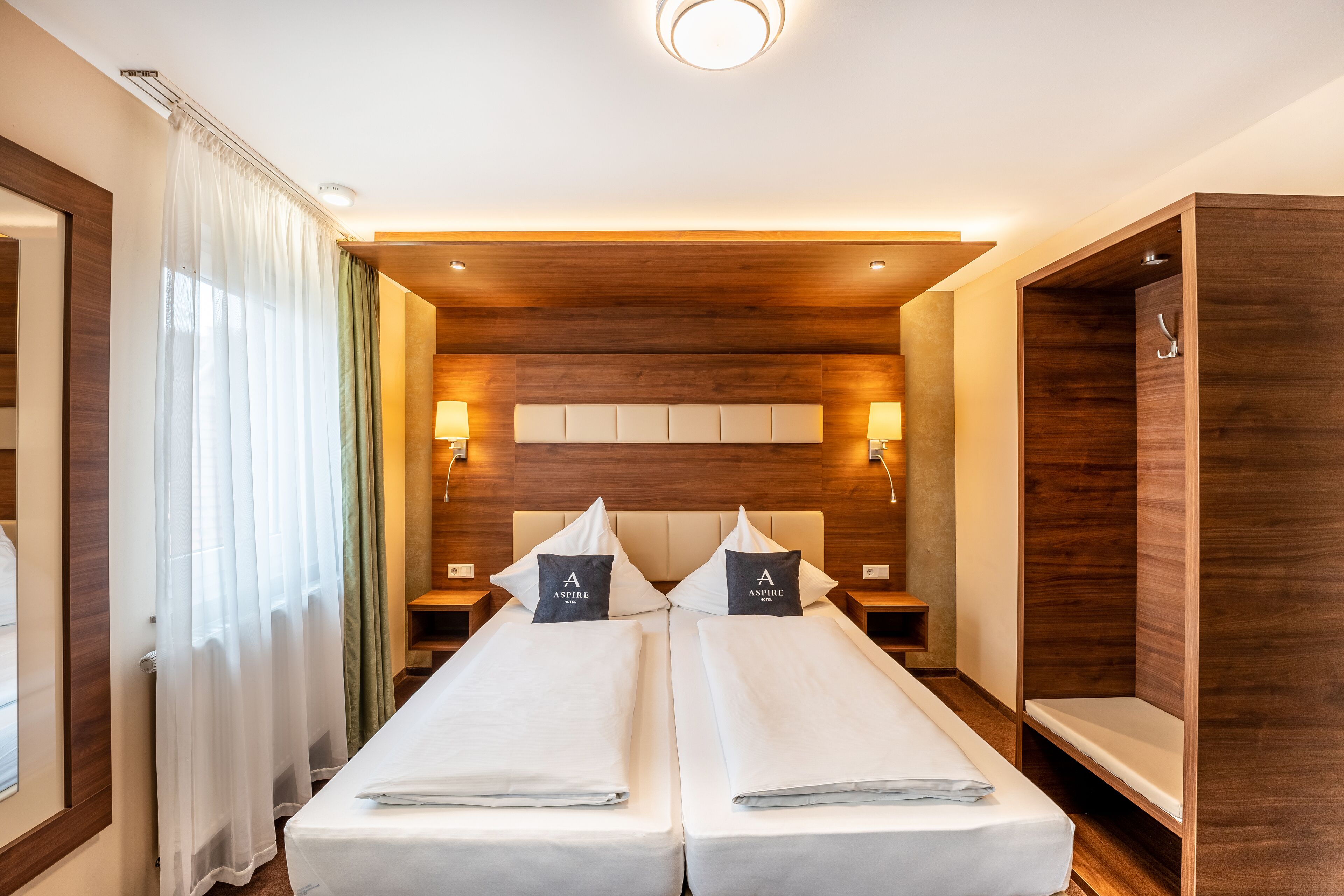 Une chambre double avec deux lits, une tête de lit en bois, des lampes de chevet et une banquette intégrée.