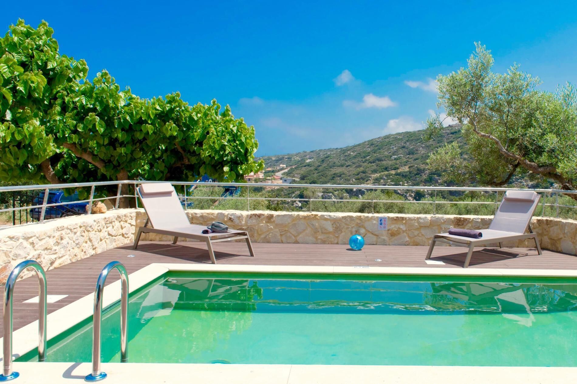 Una zona de piscina con dos sillones de relax y un muro de piedra.