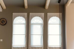 Three arched windows with a curtain, a clock on the wall, and wooden beams on the ceiling. - Villa Murtal (Rethymno)