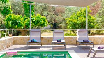 Una piscina al aire libre, sombrillas, sillones reclinables de piscina