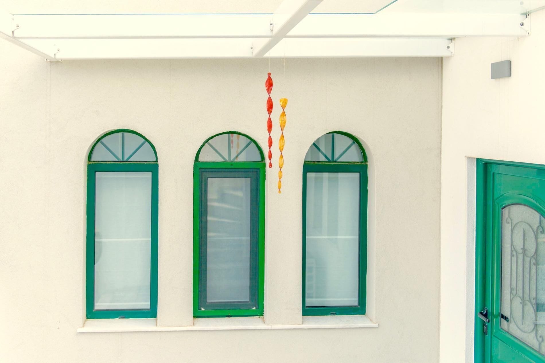 Fachada de edificio con tres ventanas arqueadas de marcos verdes, una puerta de marco verde y un adorno colgante.