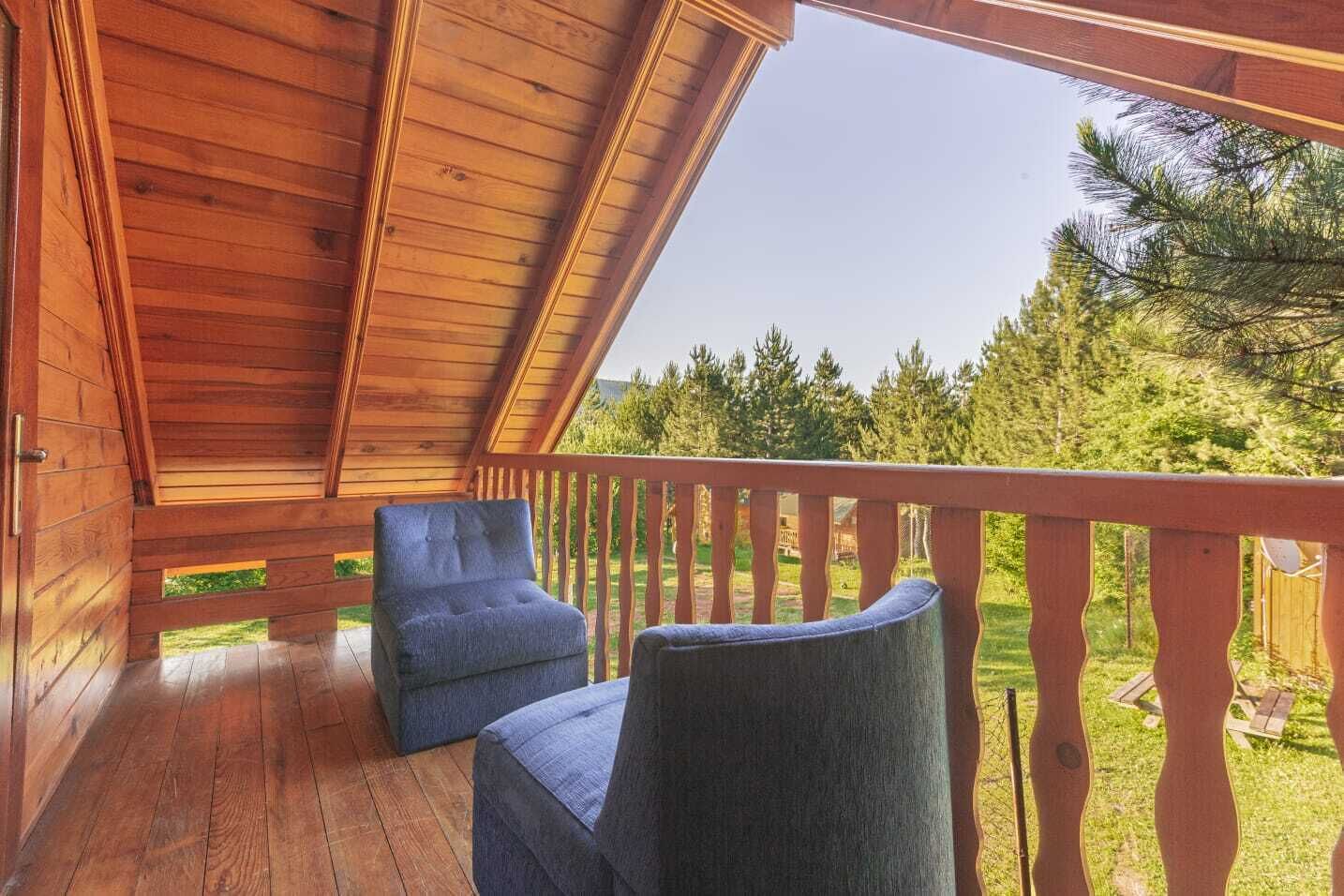 Une terrasse en bois avec deux chaises bleues, une rambarde en bois et une vue sur une forêt.