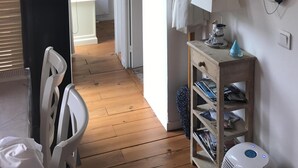 Un pasillo con suelo de madera, una silla blanca, un estante con chalecos salvavidas y una mesita con objetos decorativos.