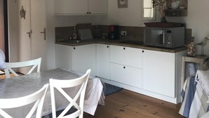 Una cocina compacta con armarios blancos, una mesa de comedor con sillas y piso de madera.