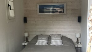 Un dormitorio con cama, dos lámparas de noche, un cuadro enmarcado en la pared y una puerta con picaporte.