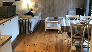 Una sala de estar acogedora con suelo de madera, un sofá, una mesa de centro y un comedor con sillas.