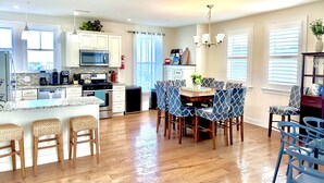 A modern kitchen with a central island, wooden bar stools, and a dining table with patterned chairs. - STEPS TO BEACH & BOARDWALK. 5BR/3BATH. Private Elevator! (Ocean City)