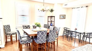 A dining area with a wooden table and chairs, a chandelier, and a vase with flowers. - STEPS TO BEACH & BOARDWALK. 5BR/3BATH. Private Elevator! (Ocean City)