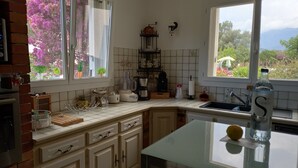 A kitchen with white cabinets, a brick oven, and a window with a view of flowers and mountains. - House, pool, haven of peace   (Prunelli-di-Fiumorbo)