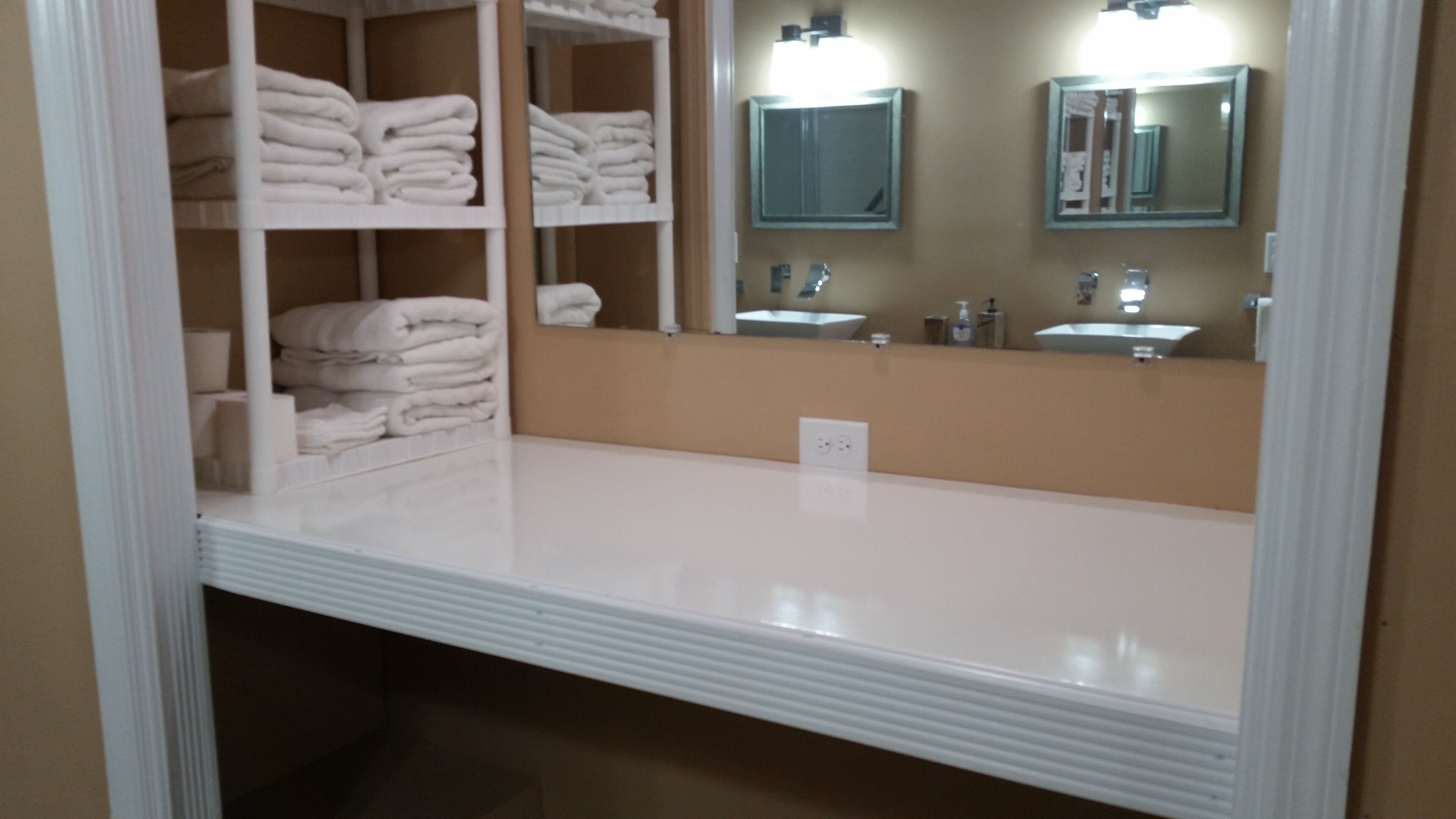 Un baño con tocador blanco, espejo y repisas con toallas dobladas.