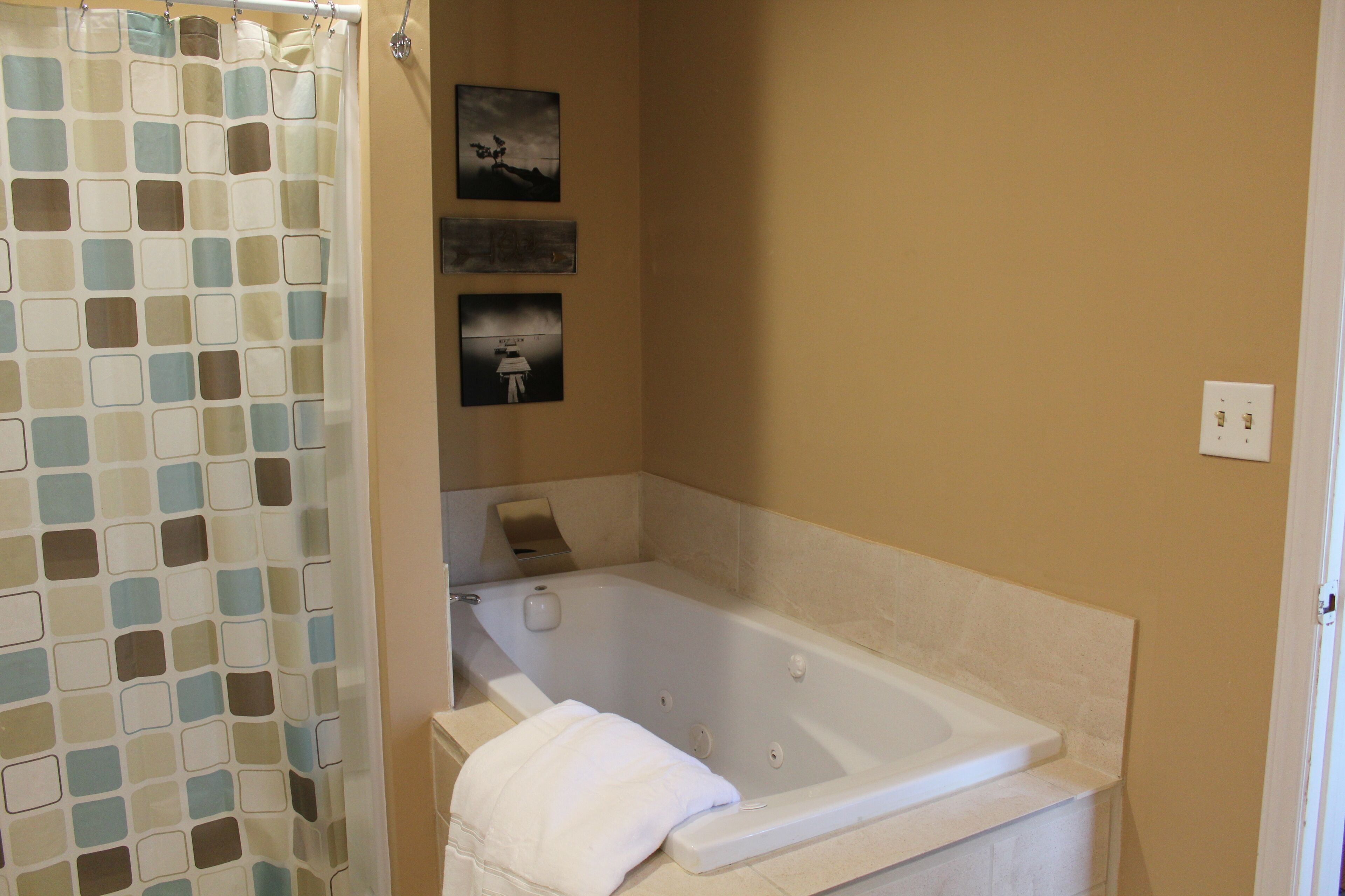 A bathroom with a bathtub, a shower curtain, and three framed pictures on the wall.