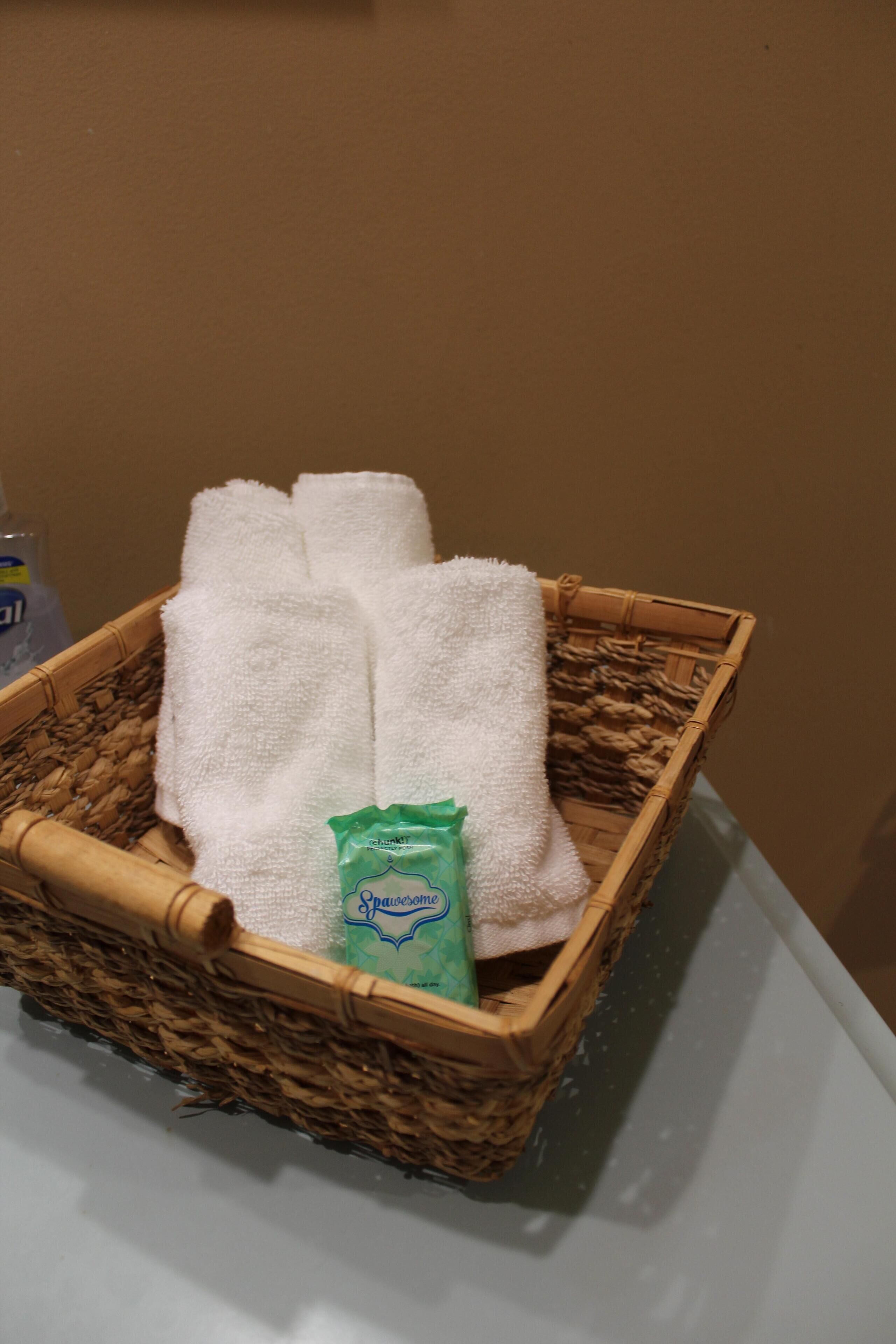 A wicker basket containing white towels and a green bottle on a white surface.