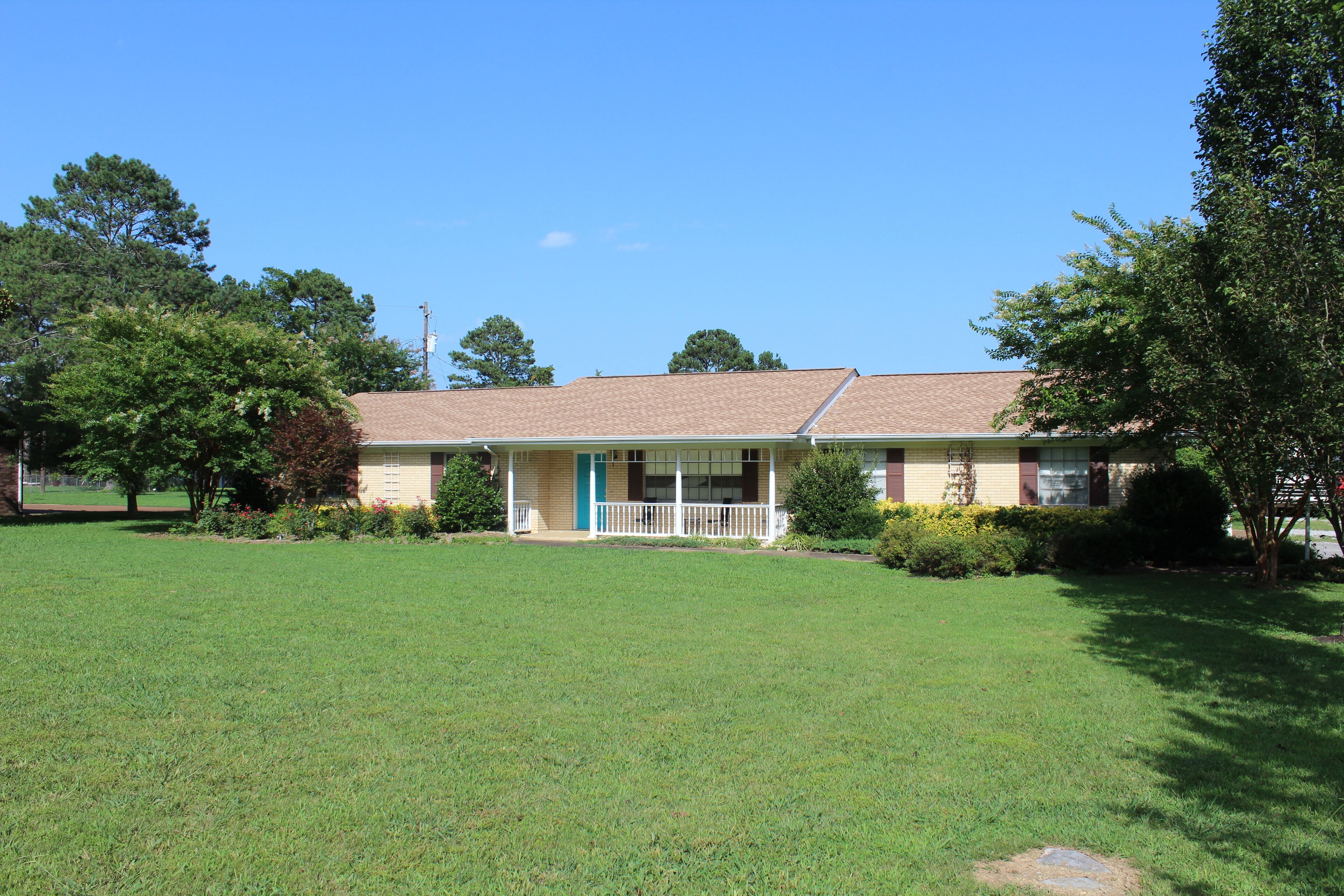 A single-story house with a front porch, a lawn, and surrounding trees.