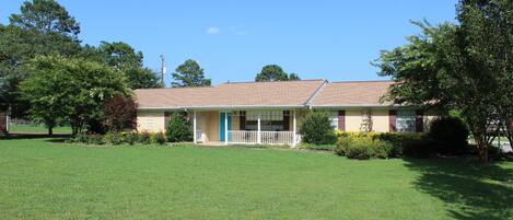 A single-story house with a front porch, a lawn, and surrounding trees.