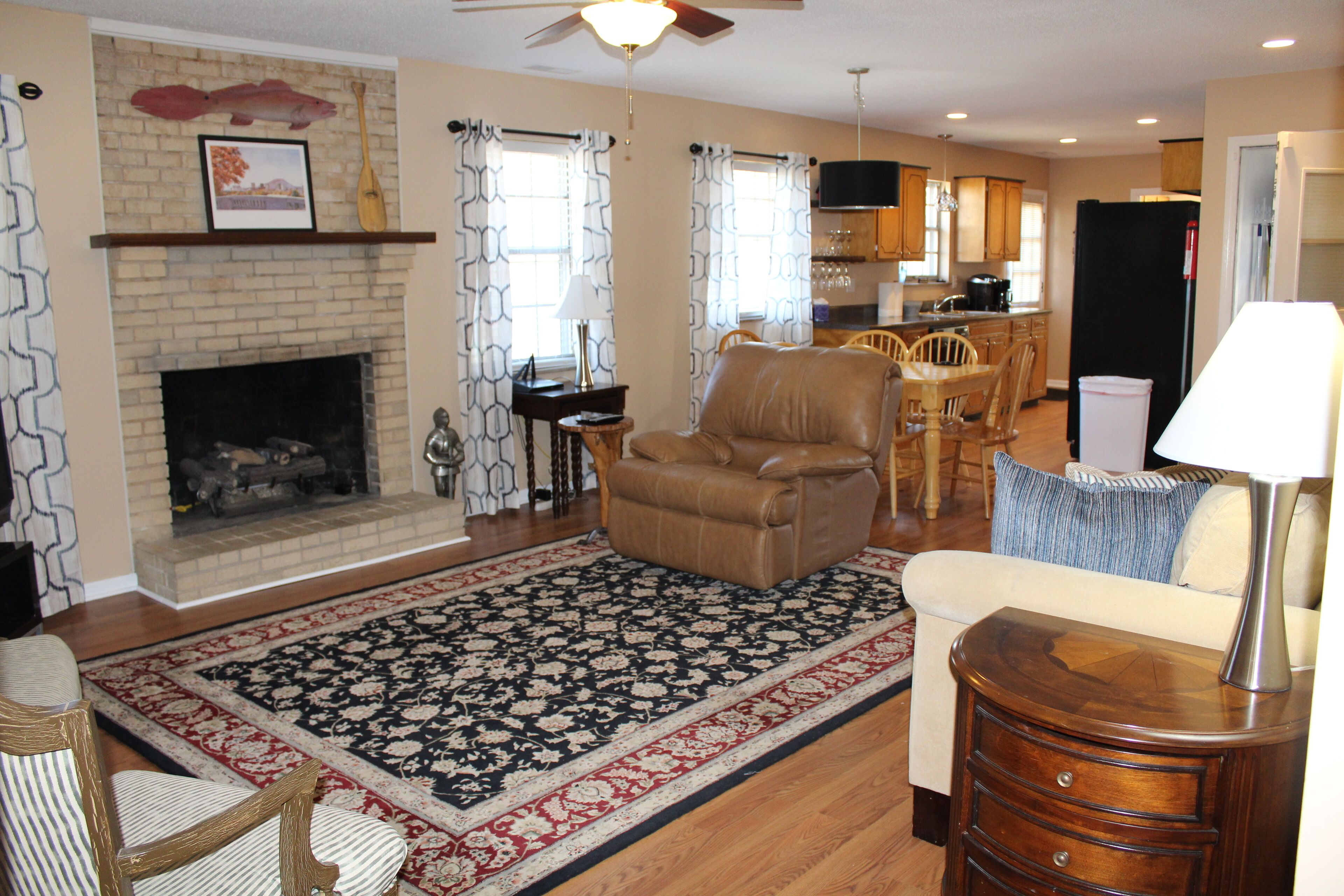 A living room with a fireplace, a dining area with a table and chairs, and a kitchen in the background.