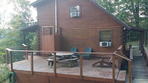 Una cabaña de madera con terraza, mobiliario exterior y una escalera que conduce al nivel superior.